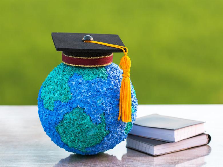 A small globe with a graduation cap on top of it sitting next to a pile of books